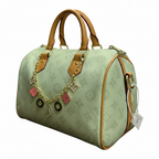 A Louis Vuitton monogrammed light green duffel bag with tan leather trim, gold-tone hardware, and a decorative gold chain charm with pink and black accents, shown on a plain white background.