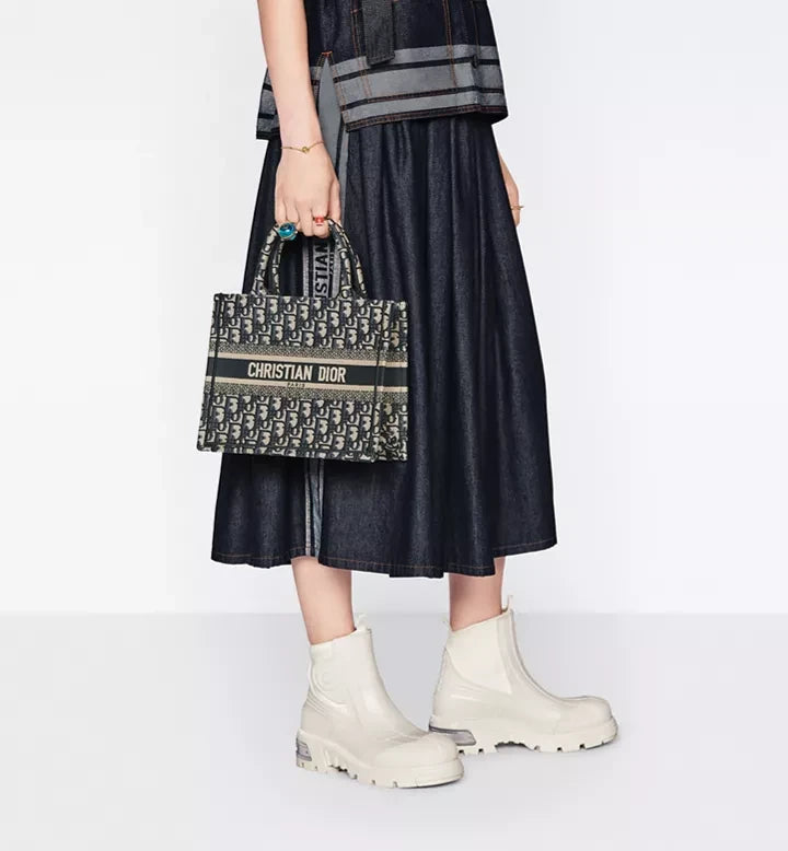 MOAH Christian Dior small book tote in navy and beige embroidered Oblique canvas held by a model in a denim skirt.