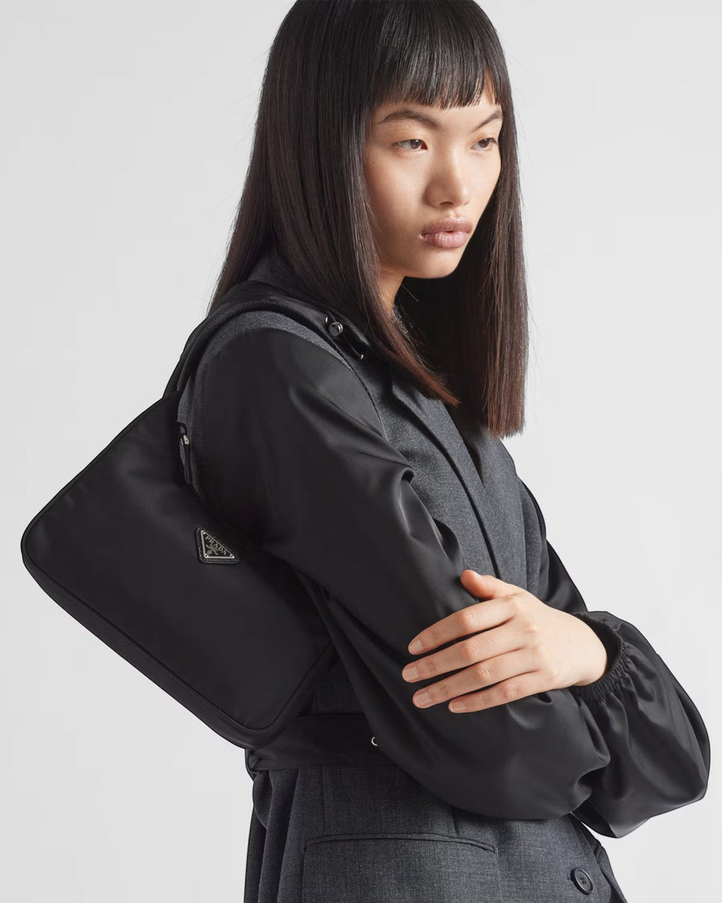 MOAH Prada Re-Edition 2000 black Re-Nylon mini bag with enameled metal triangle logo worn over the shoulder by a model