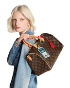MOAH shoes model carrying a brown Louis Vuitton Speedy Bandouliere handbag with monogram canvas and gold hardware.