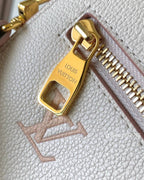 Close-up of a Louis Vuitton handbag in light beige pebbled leather with a gold-tone zipper pull engraved with 'LOUIS VUITTON'.