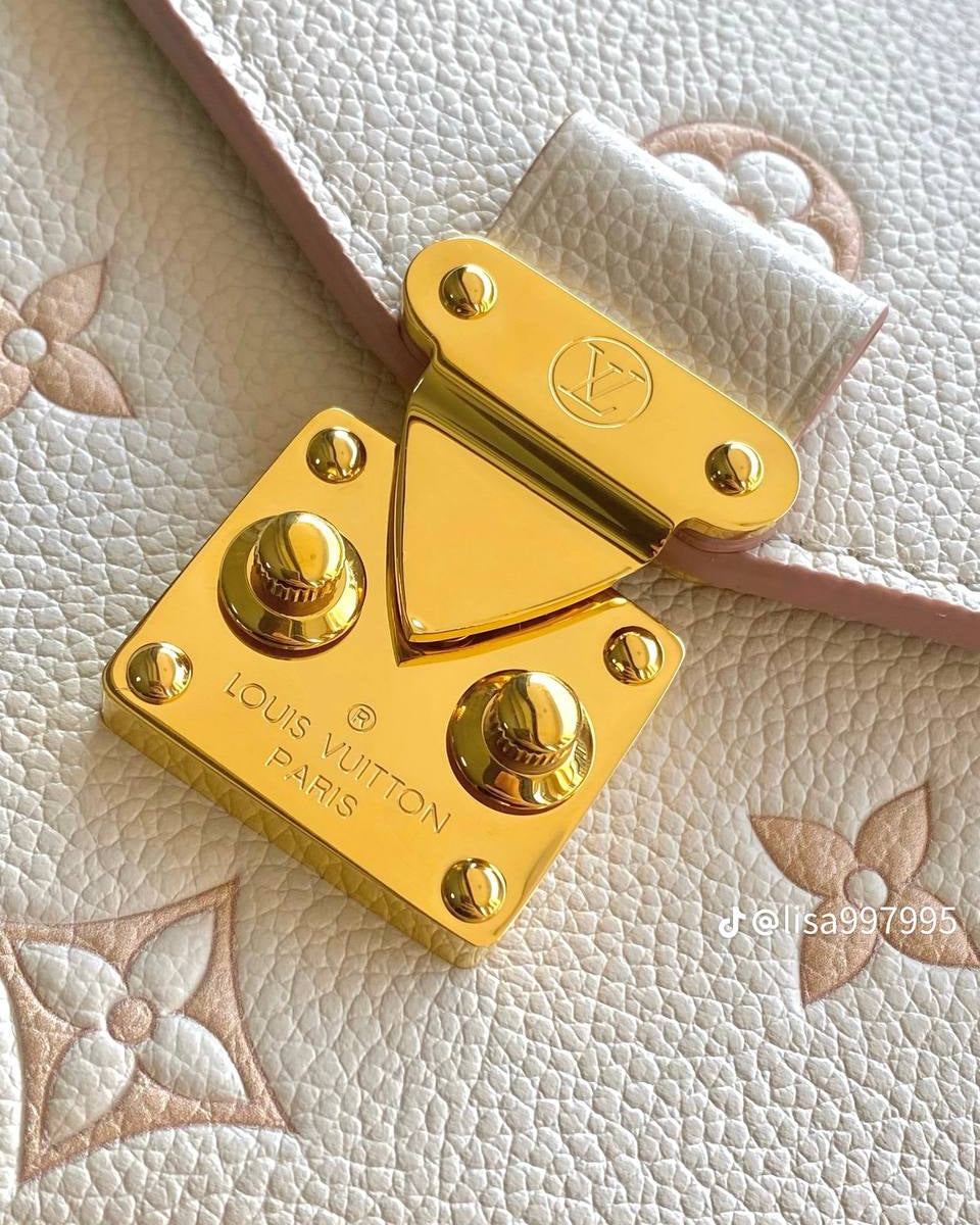Close-up of a Louis Vuitton handbag clasp in polished gold-tone metal, mounted on a light beige textured leather strap with embossed monogram pattern.